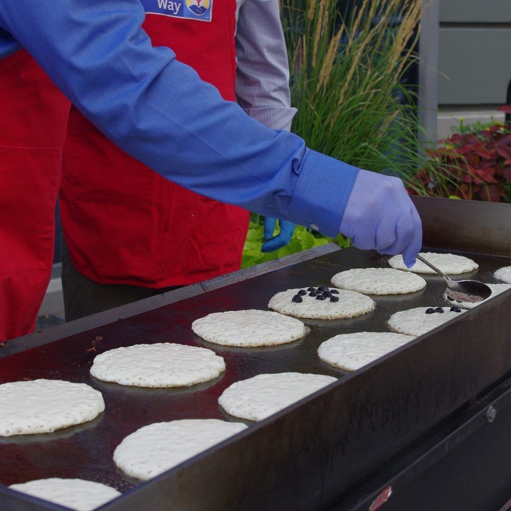 Cooks with gloves and red aprons at a pancake griddle