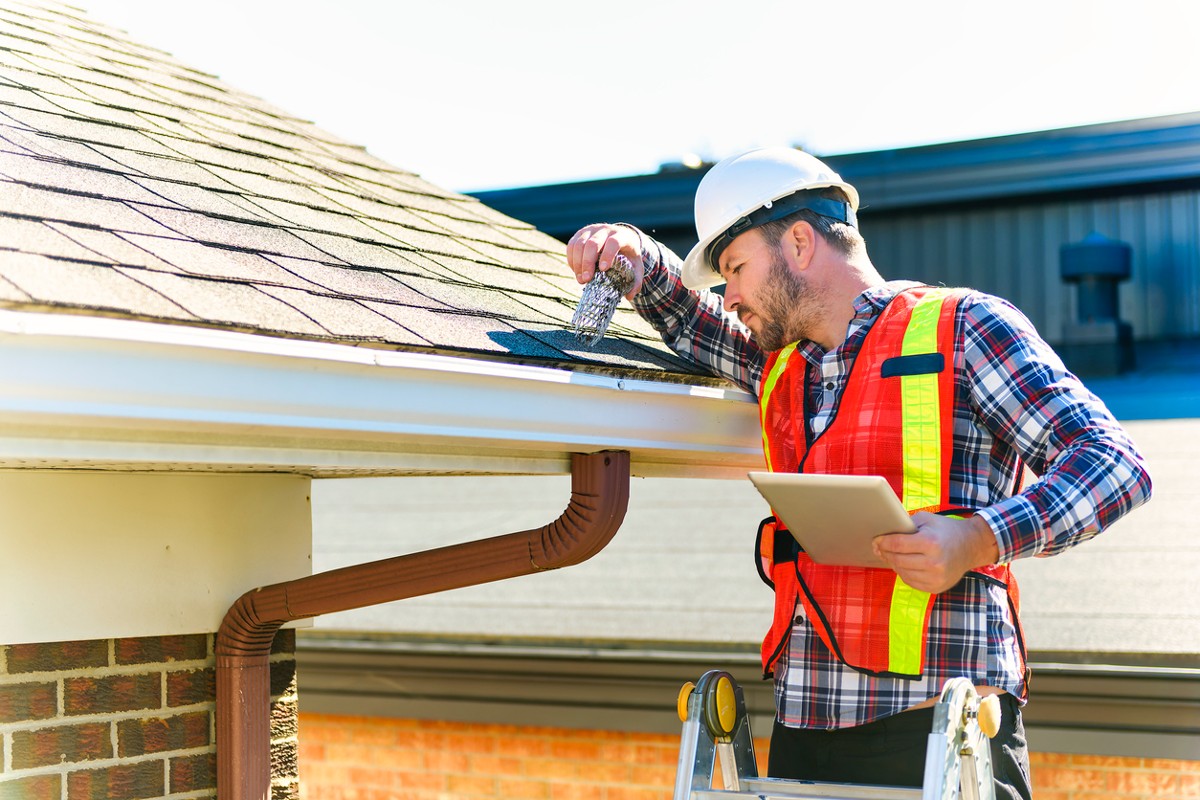 Man with hard hat standing on steps inspecting house roof for asbestos
