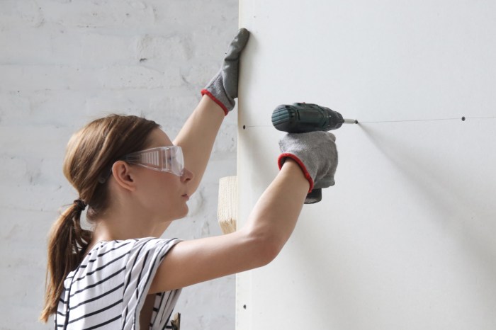 Young woman drilling screws into plasterboard with an electric screwdriver, home improvement concept