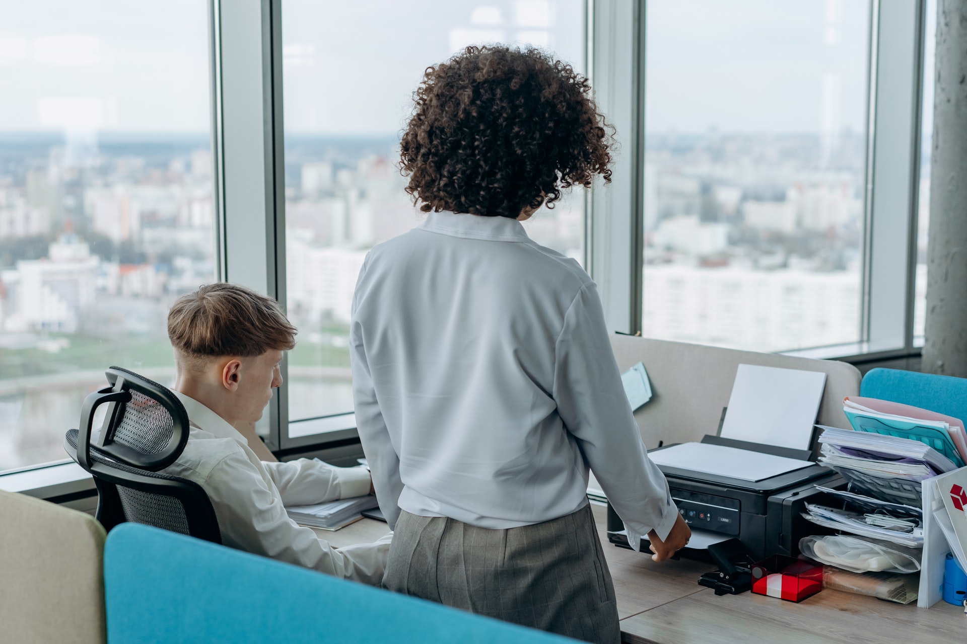 Two people at a desk with a copy machine/printer