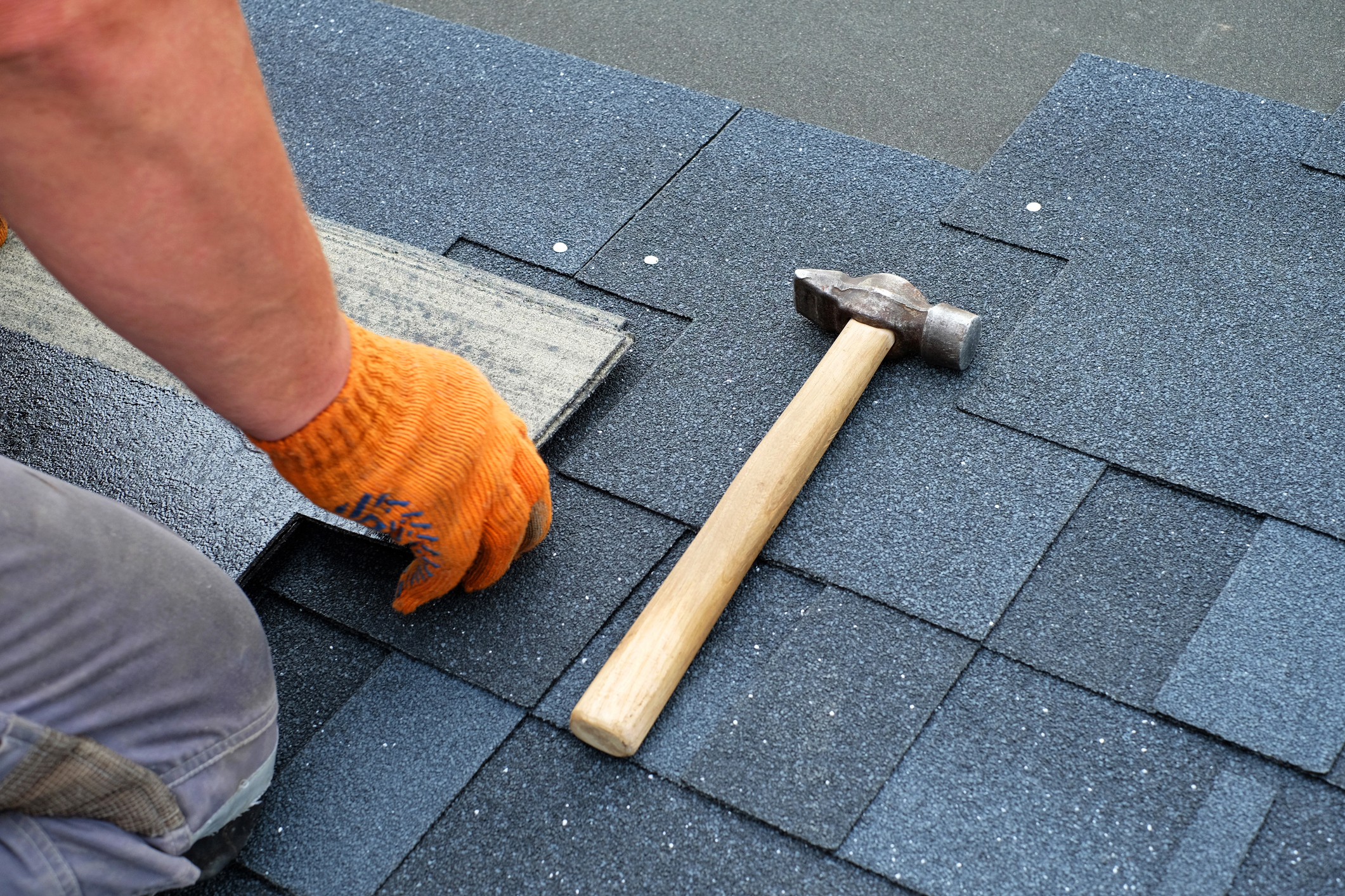 Hammer and nails installing shingles on a roof