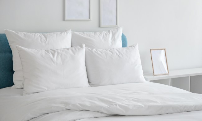 A white bed with pillows and a duvet in front of a white wall