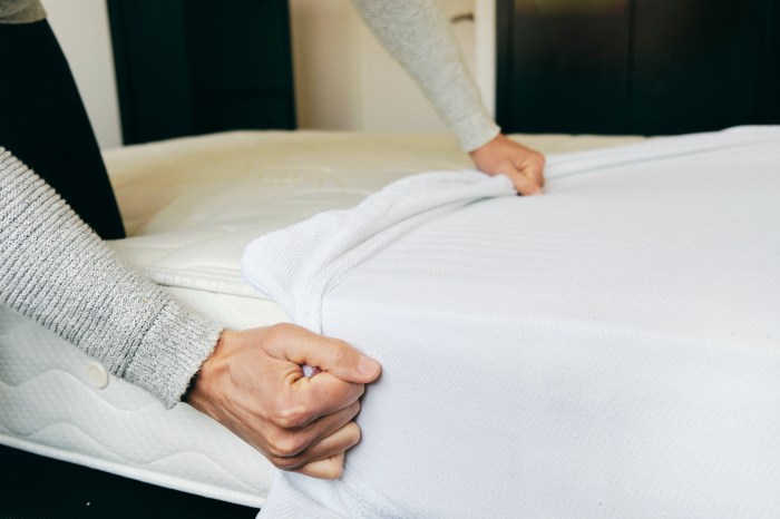 Hands hold a mattress protector and pull it over a matress