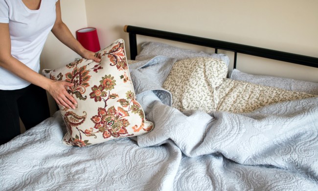 A woman holds a pillow while making the bed
