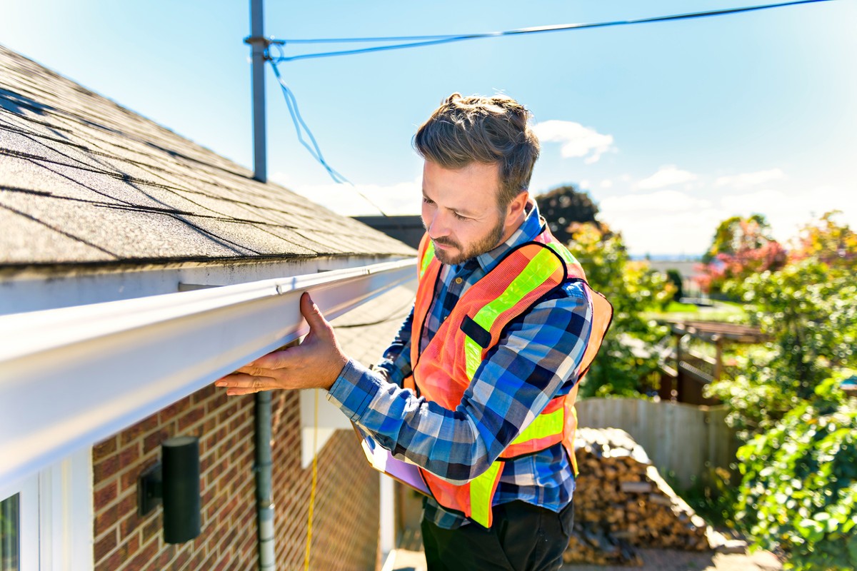 Man with hard hat standing on steps inspecting house roof for asbestos