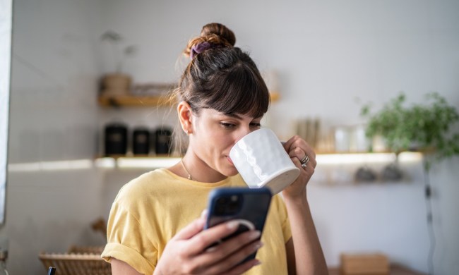 Young woman using the mobile phone while drinking coffee or tea at home